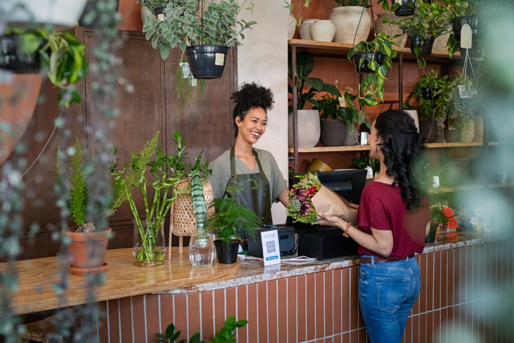 Happy florist selling plants and flowers to client standing at the point of sale